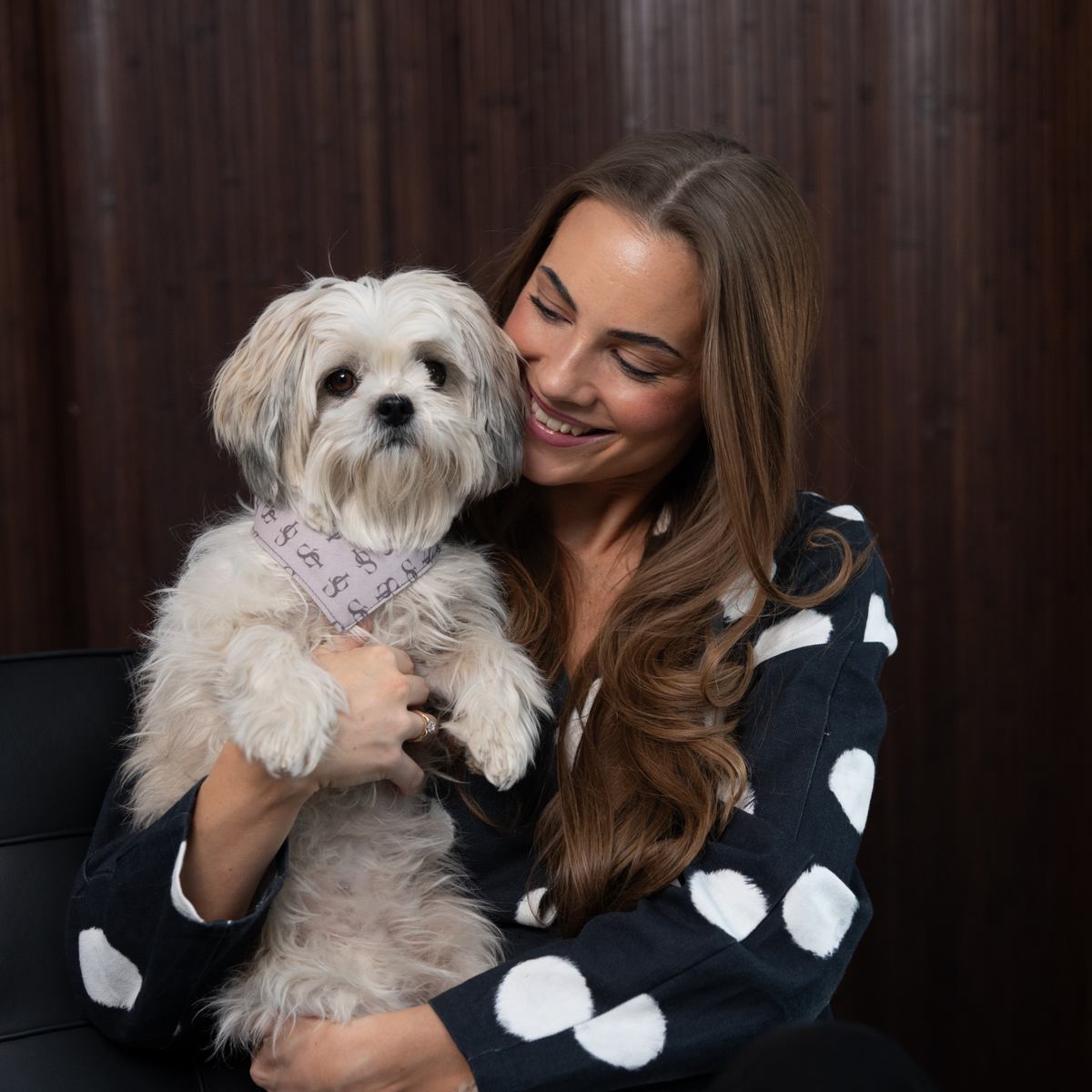 En kvinde i en cardigan med prikker, der holder en shih tzu, der har en Staey-Bandana på