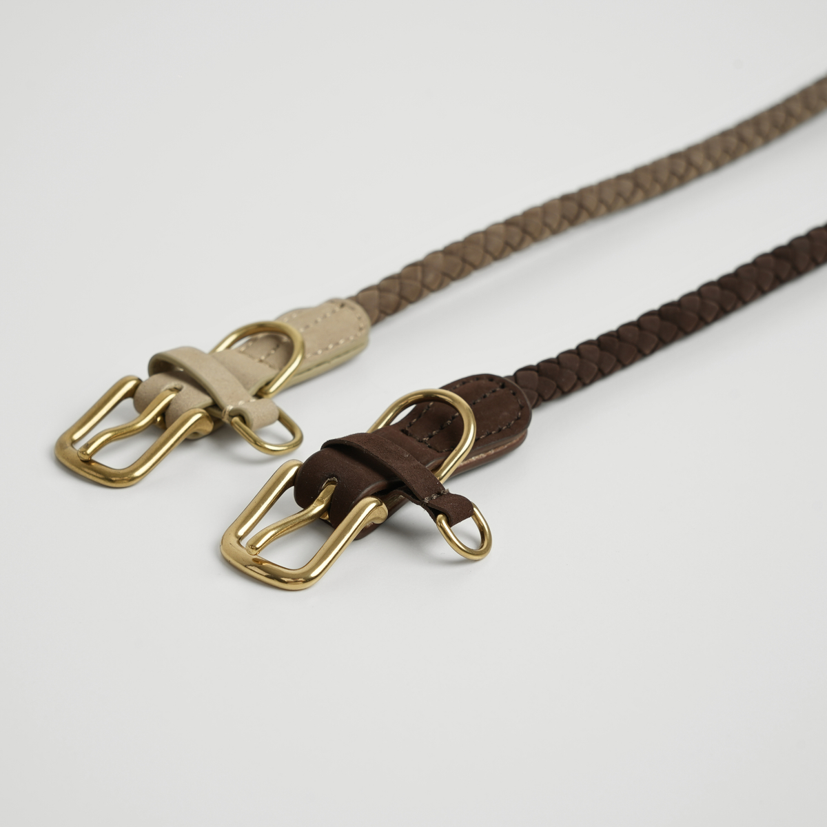 Two braided leather dog leashes in taupe and dark brown with brass hooks