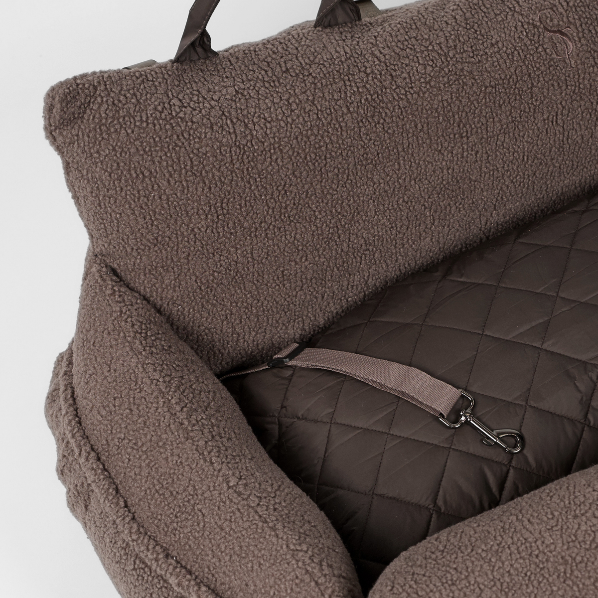 The Clara teddy car seat opened, showing the quilted lining and safety strap