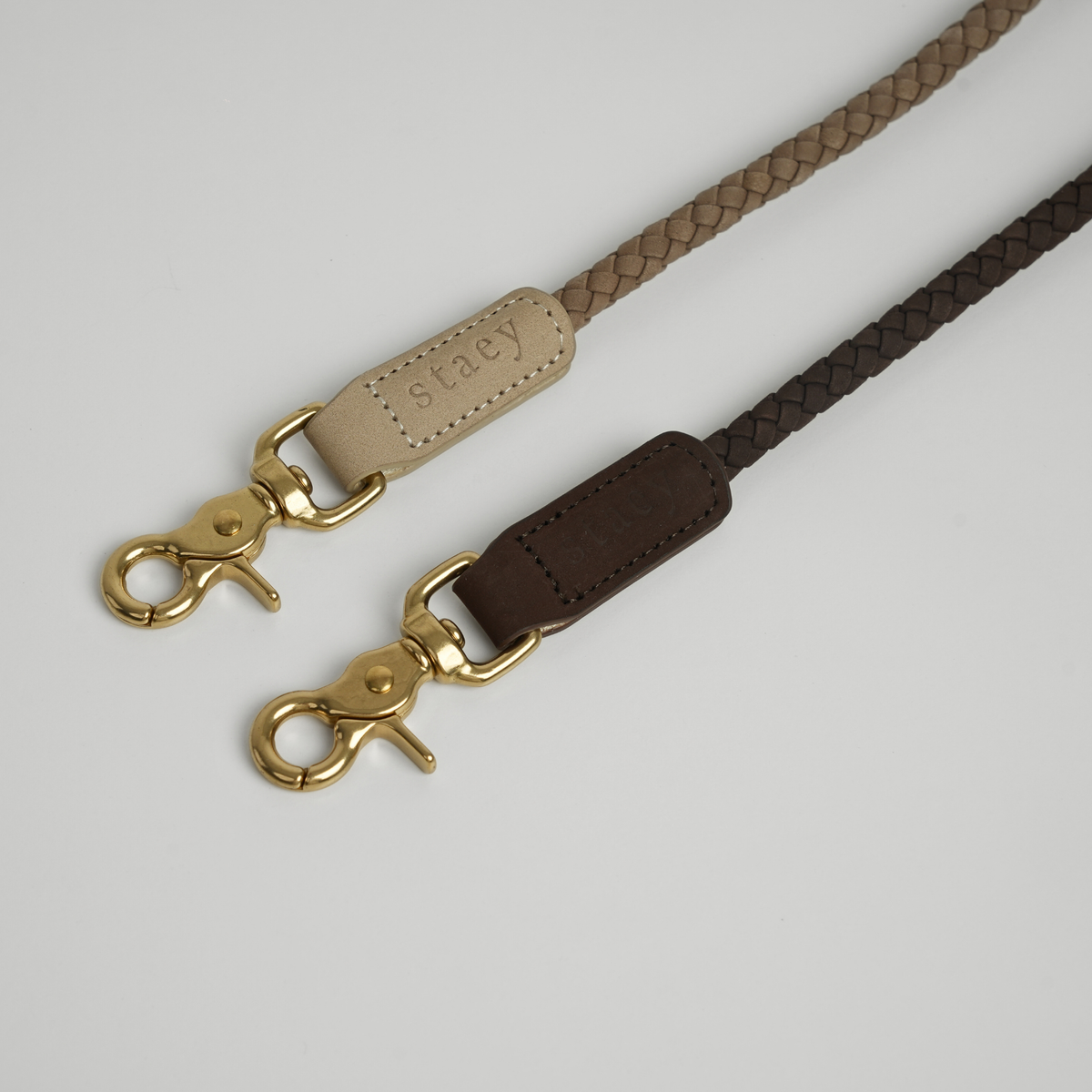 Two braided leather leashes in taupe and dark brown with brass hooks