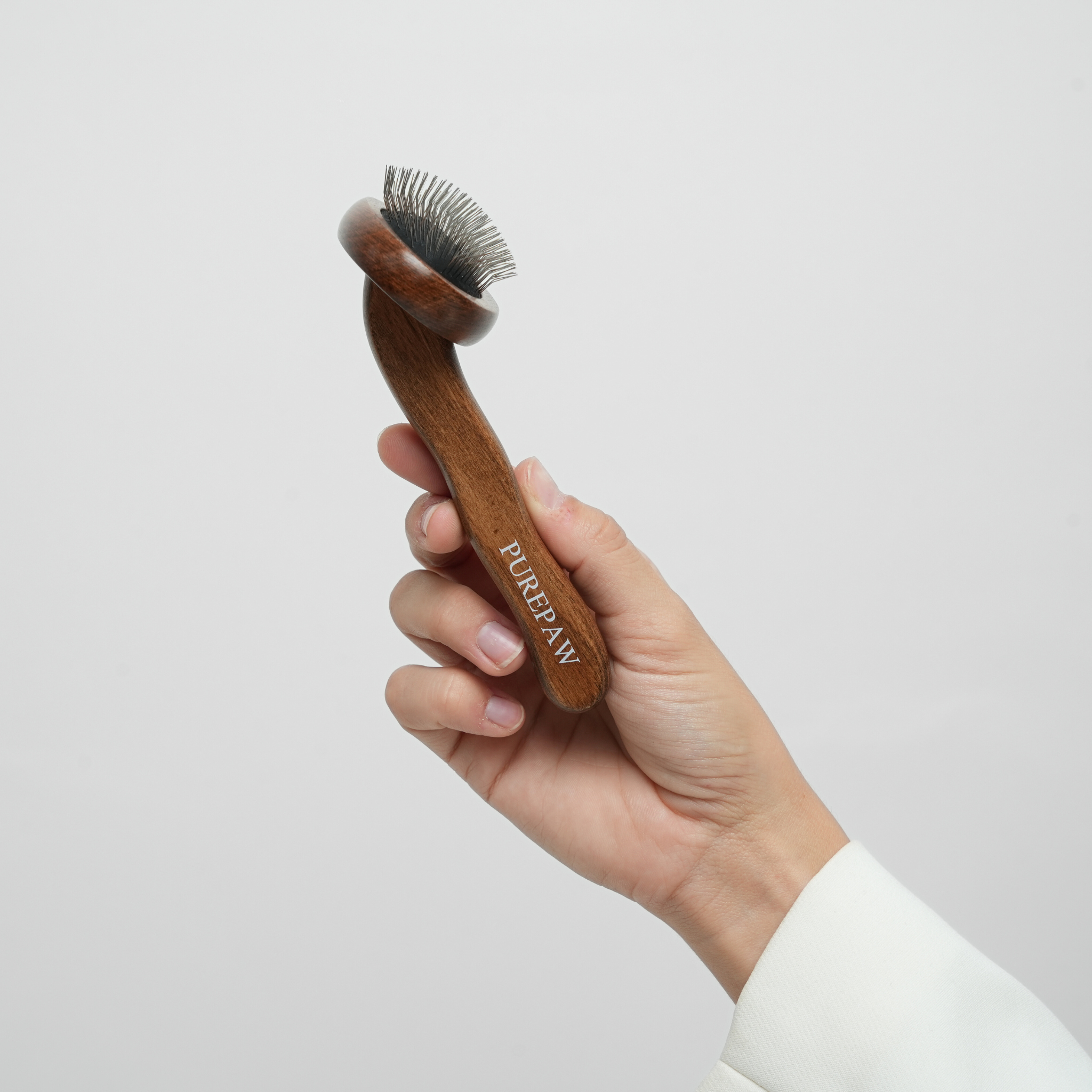 Hand holding a wooden dog grooming brush with 'Purepaw' branding against a light gray background