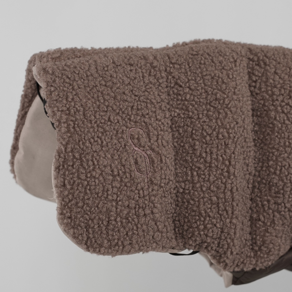 Nærbillede af det prægede Staey-monogram på den taupefarvede teddy-hundefrakke