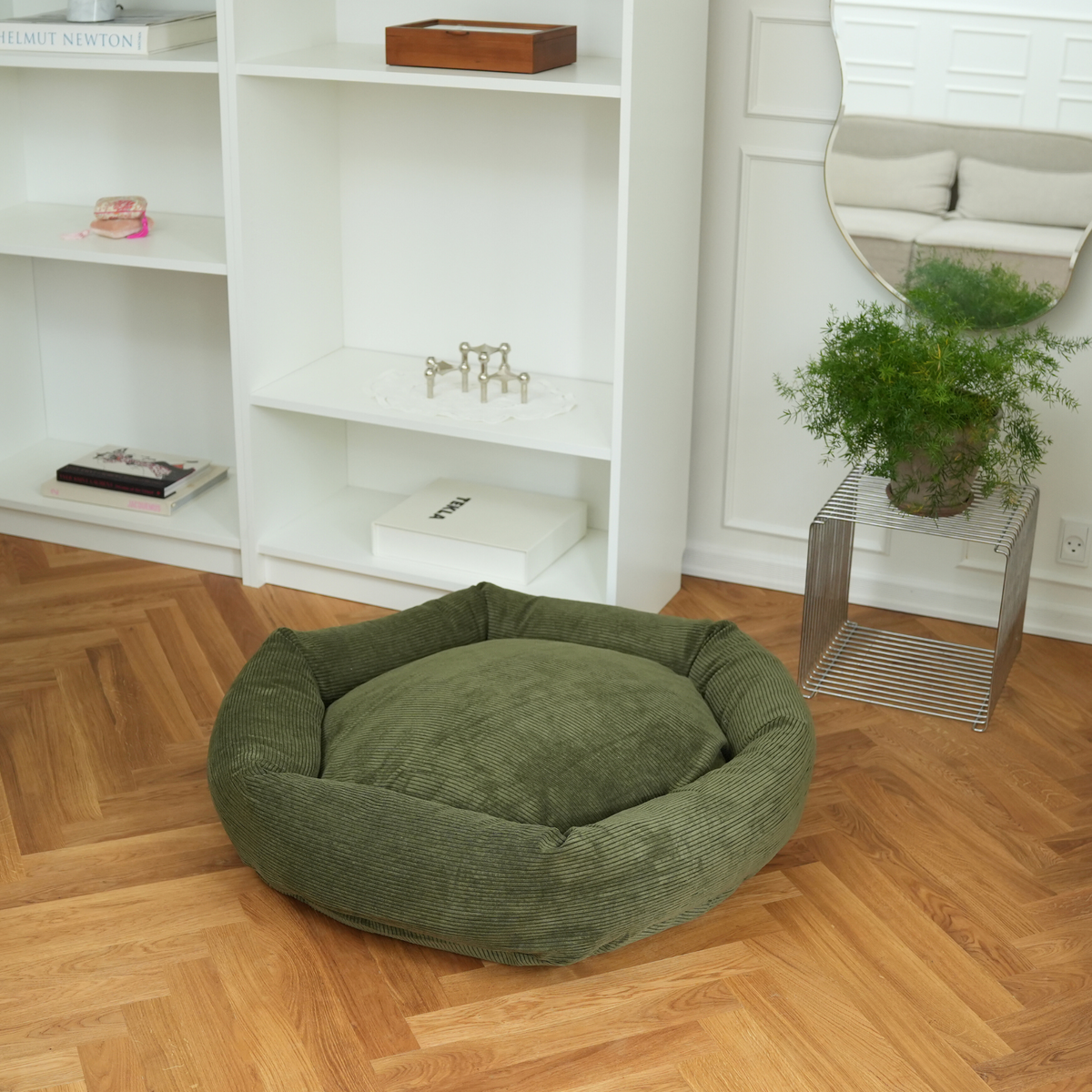 The moss green corduroy dog bed on a parquet floor in a living room