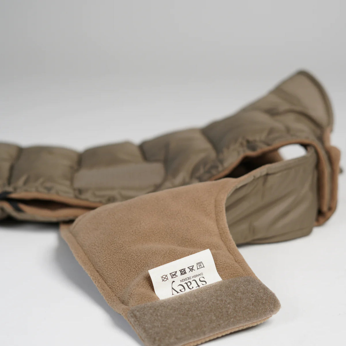 The taupe quilted dog coat laid flat, showing its fleece lining and label