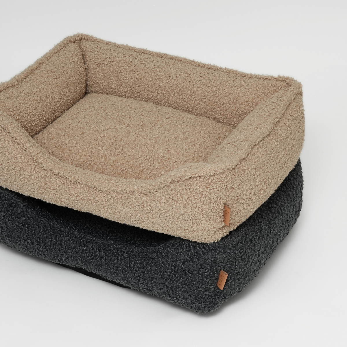 Two curly bouclé dog beds stacked in sand and storm