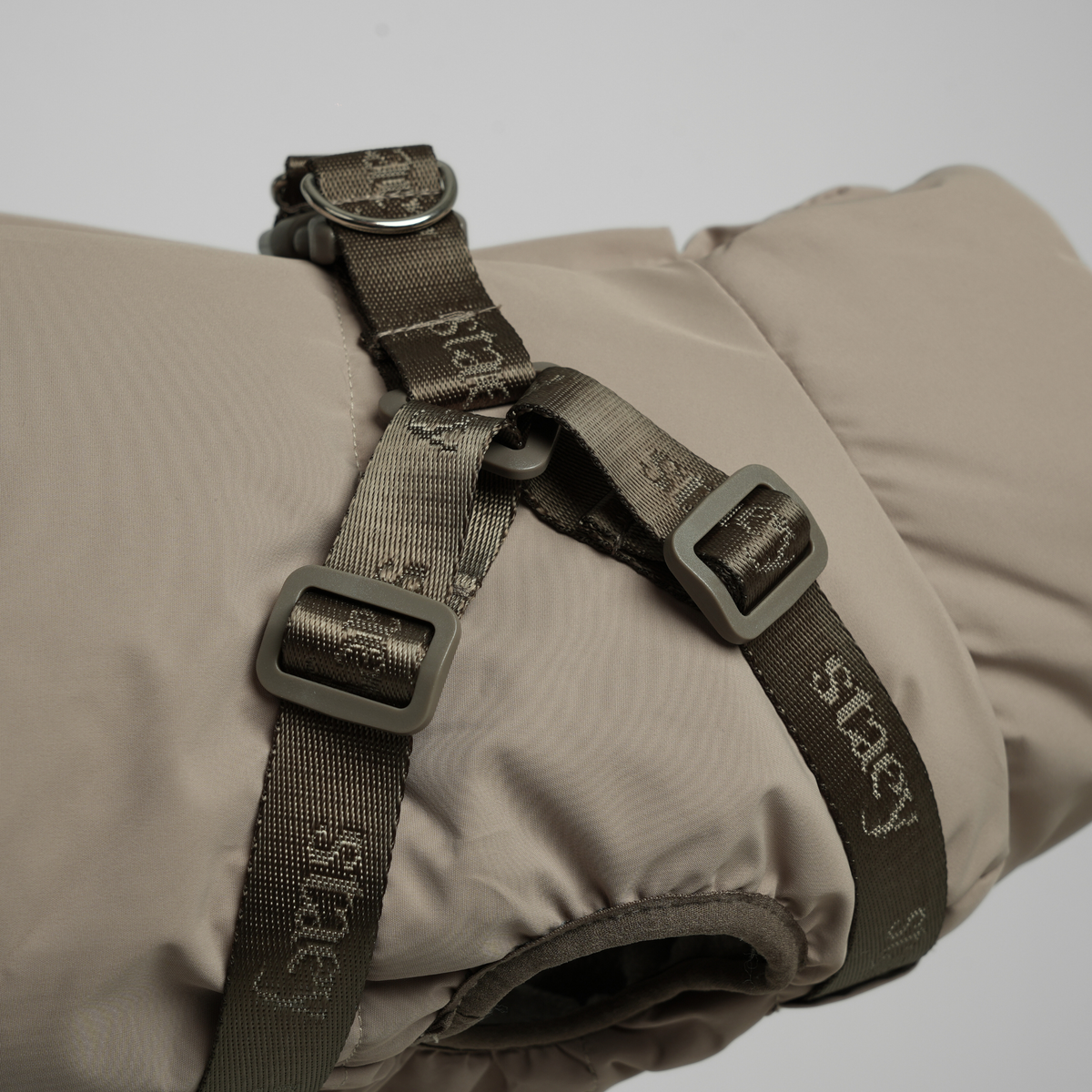 Close-up of the harness buckles and webbing on the taupe quilted coat