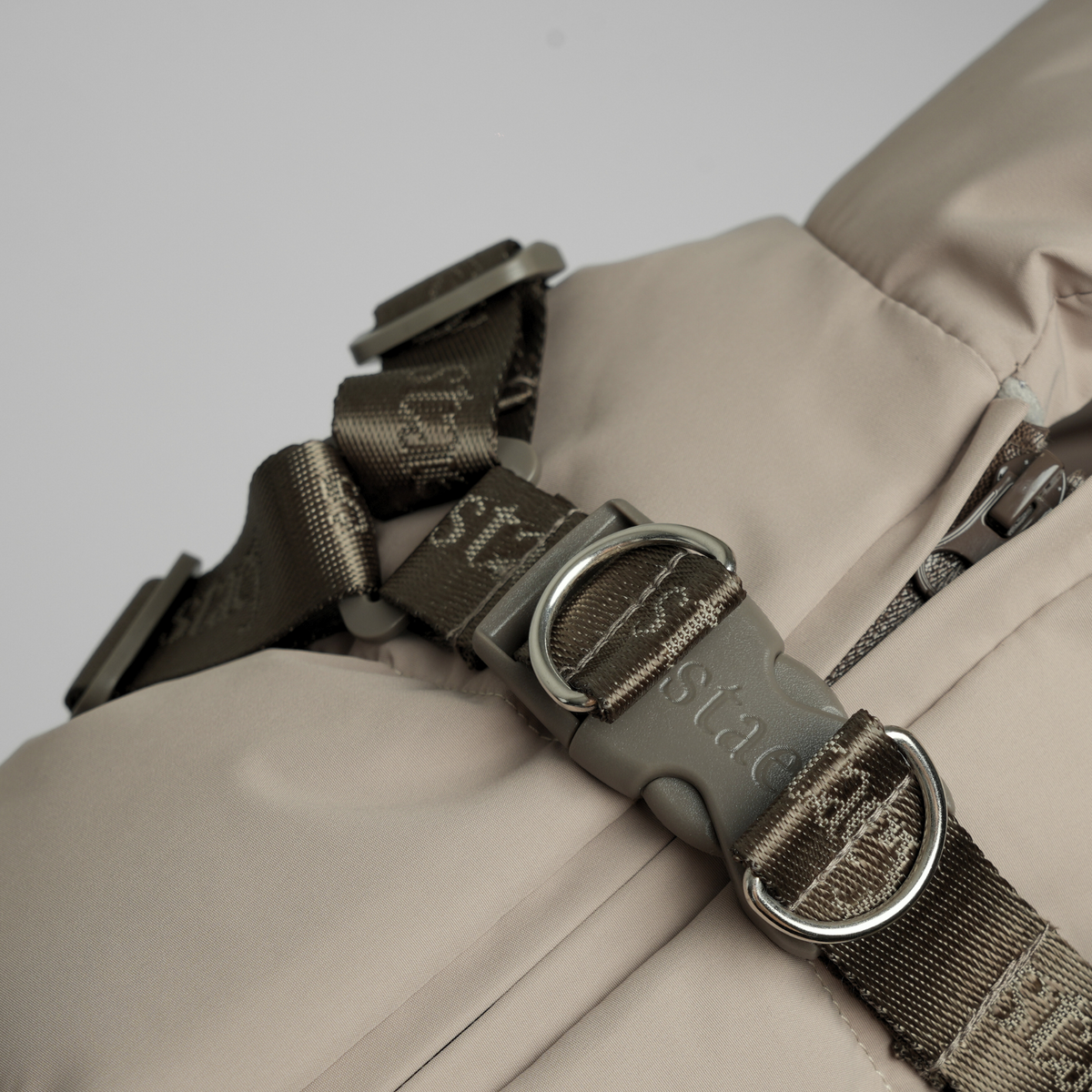Close-up of the harness buckle and webbing on the taupe quilted coat