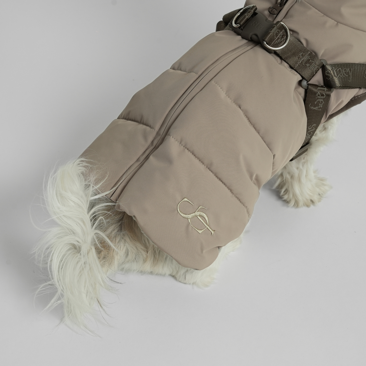 Close-up of the taupe quilted coat and harness on a white dog's back