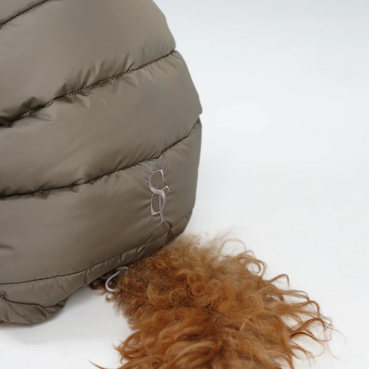 Close-up of the embossed Staey monogram on the taupe quilted coat
