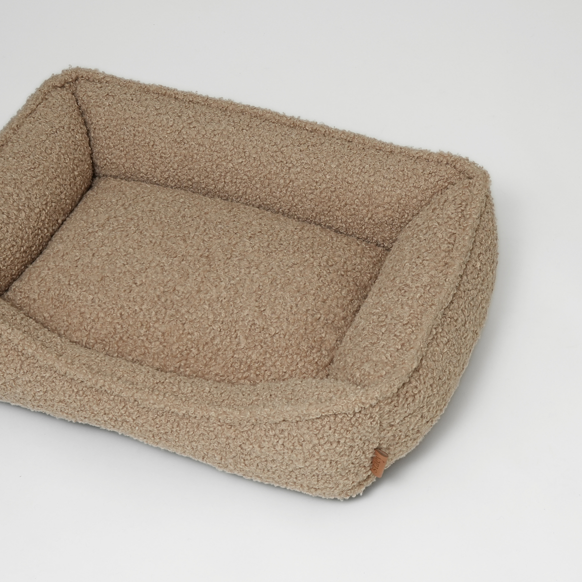 The sand curly bouclé dog bed seen at an angle