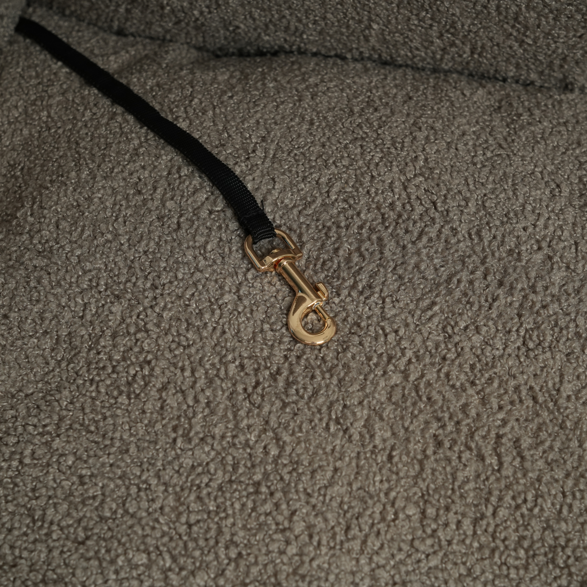 Close-up of the safety leash with a brass hook inside the taupe bouclé car seat